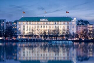 Historisches Hotel Atlantic in Hamburg, beleuchtet am Abend, mit Spiegelung im Wasser.