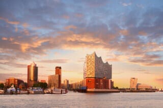 Hamburgs Skyline bei Sonnenuntergang mit der Elbphilharmonie und Hafenbooten im Vordergrund.