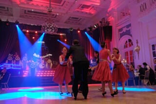 Tanzende Paare in roten Kleidern bei einem festlichen Ball in eleganter Umgebung.