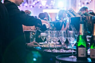 A waiter pours champagne into glasses at a festive event with a glamorous ambience.