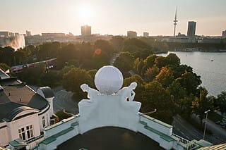 Blick auf die Alster mit Skulpturen und der Skyline von Hamburg bei Sonnenuntergang.