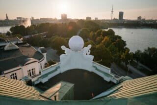View from above of the building with figures and a view of the city of Hamburg at sunset.