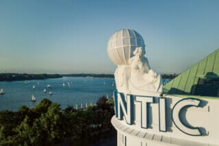 Blick auf den See mit Segelbooten und der historischen Statue auf dem Gebäude im Vordergrund.