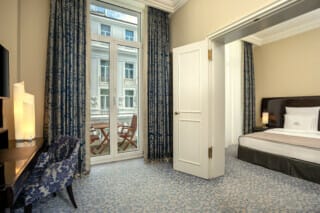 Elegant hotel room with balcony, blue curtains and stylish furnishings.