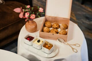 Scones in Holzbox mit Beerenmarmelade, Sahne und frischem Obst auf einem Tisch dekoriert.