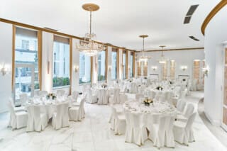 Elegant function room with round tables and chandeliers in a bright ambience.