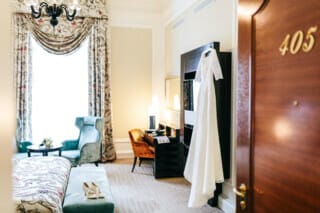 Elegantes Hochzeitskleid hängt in einem stilvollen Hotelzimmer mit gemütlicher Einrichtung.