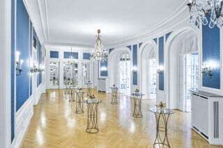 Eleganter Raum mit blauen Wänden, Kristalllüstern und Stehtischen für Veranstaltungen.