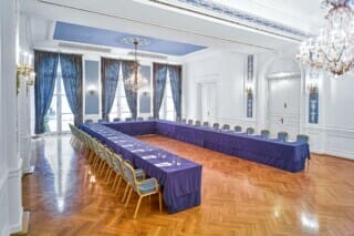 Eleganter Konferenzraum mit langer Tafel, blauen Vorhängen und Kronleuchtern.