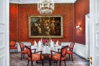 Eleganter Speisesaal mit roter Wand, antikem Gemälde und stilvollen Stühlen.