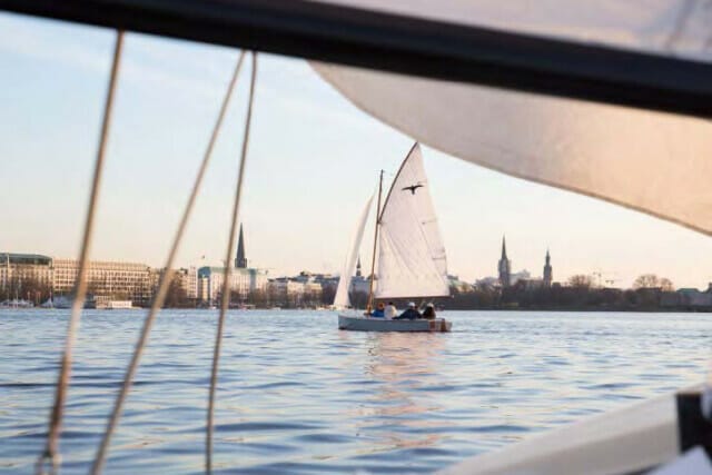 Segelboot auf ruhigem Wasser mit Hamburger Skyline im Hintergrund bei Sonnenuntergang.