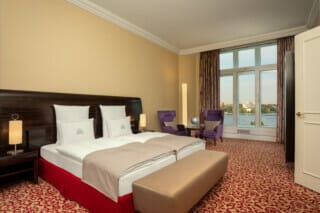 Modern hotel room with double bed, cosy armchairs and a view of the river.