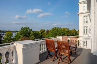 Balcony with wooden furniture and view of the green garden and the watercourse in the background.