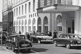 Eingang des Atlantic Hotels mit klassischen Autos und Fußgängern in der Innenstadt.