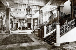 Elegant hotel lobby with staircase, chandeliers and stylish furniture in historical design.