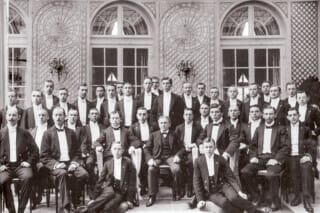 Historisches Gruppenfoto von Männern in Anzügen, aufgenommen in einem eleganten Raum.