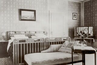 Historisches Schlafzimmer mit zwei Betten, Sofa, Spiegel und dekorativen Elementen.