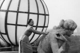 Frau steht auf einer Leiter neben einer Statue und einer großen Glaskugel im Hintergrund.