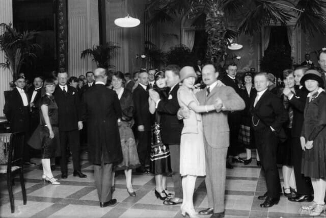 Tanzende Paare in eleganter Kleidung bei einer Veranstaltung in den 1920er Jahren.
