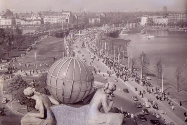 Blick auf eine belebte Promenade mit historischen Statuen und einem Fluss im Hintergrund.