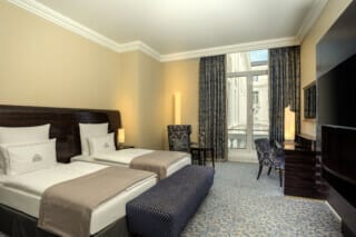 Elegant hotel room with two beds, desk and view of the city.