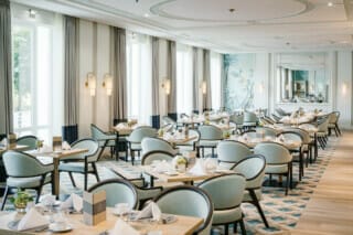 Eleganter Restaurantbereich mit hellen Fenstern, stilvollen Tischen und modernen Stühlen.