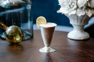 Eleganter Cocktail in einem silbernen Glas mit Zitrone, dekoriert auf einem Holztisch.