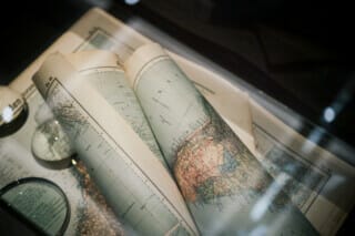 Historische Landkarten und Lupe in einer Vitrine, detailreiche geografische Darstellungen.
