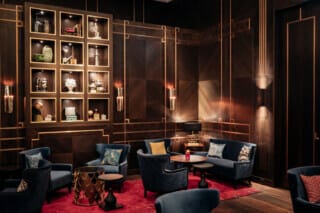 Elegantes Lounge-Interieur mit blauen Sesseln, Holzwänden und dekorativen Regalen.