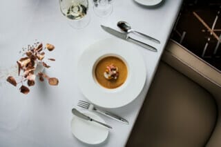 Elegantes Tischgedeck mit Suppe, Besteck und einer dekorativen Pflanze in einem Restaurant.