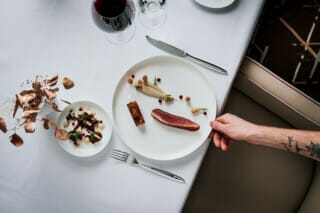 Elegantes Gericht mit Entenbrust, Beilagen und Rotwein auf einem gedeckten Tisch.