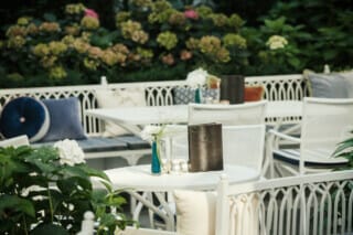 Gemütlicher Restaurantbereich mit Tischen, Blumen und Kissen in einem grünen Garten.