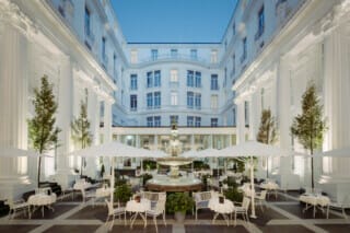 Elegant courtyard terrace with fountain, tables and parasols in a historic building.