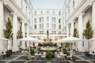 Eleganter Innenhof mit Brunnen, Tischen und Sonnenschirmen in klassischer Architektur.