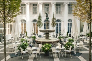 Elegante Innenhofterrasse mit Brunnen, Pflanzen und Tischen in einem historischen Gebäude.