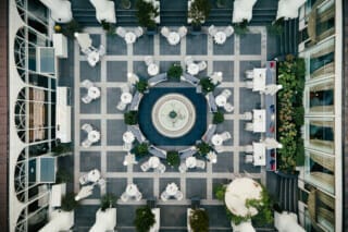 Luftaufnahme eines eleganten Innenhofs mit Tischen, Pflanzen und einem zentralen Brunnen.