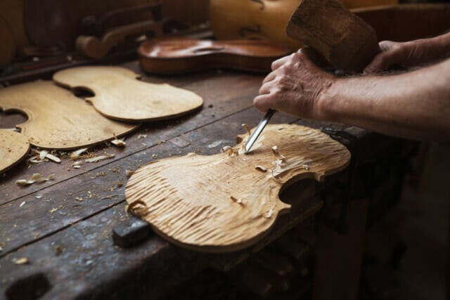 Handicraft process of violin making with wood and tools on a workbench.