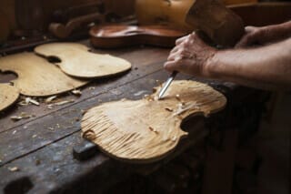 Hotel Atlantic Handwerkliche Holzarbeit: Geigenbauer schnitzt eine Holzplatte in der Werkstatt.
