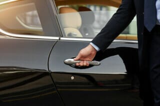 Hotel Atlantic Elegantly dressed man opens the door of a black luxury car.
