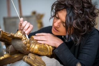 Hotel Atlantic Frau reinigt sorgfältig eine vergoldete Statue mit einem Wattestäbchen.