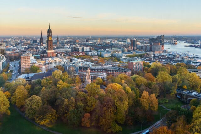 Panorama von Hamburg mit bunten Herbstbäumen und der St. Michaelis-Kirche im Hintergrund.