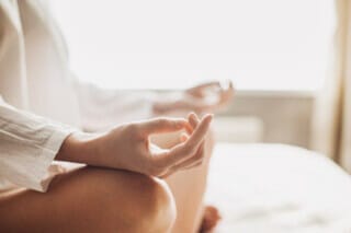 Meditation mit gefalteten Händen, entspannende Atmosphäre in einem hellen Raum.