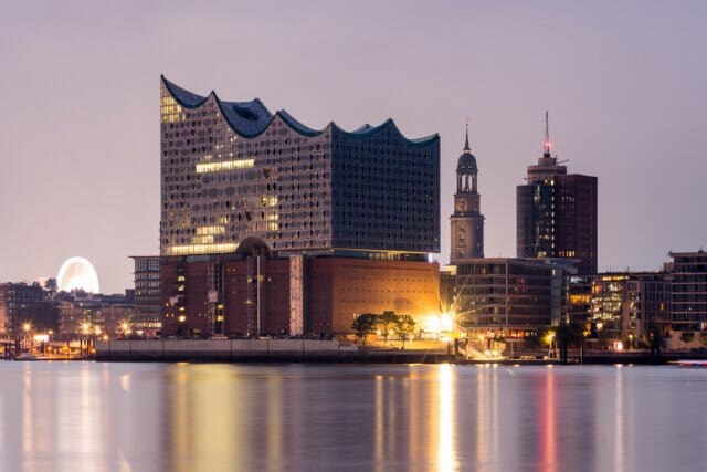 Hamburgs Elbphilharmonie bei Nacht, umgeben von modernen Gebäuden und dem Hafen.