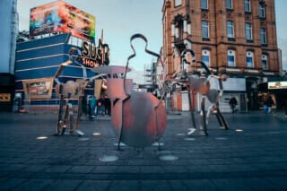 Hotel Atlantic Skulpturen von Musikern in einer Stadtstraße mit buntem Hintergrund und Menschenmenge.