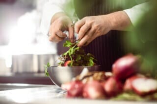 Koch bereitet frische Kräuter und Salat in einer modernen Küche vor.