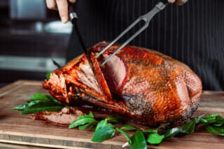 Baked duck with side dishes, red wine and stuffed apples on a festive table.