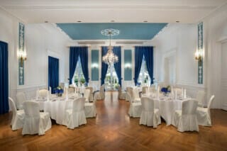 Eleganter Veranstaltungsraum mit runden Tischen, blauen Vorhängen und Kronleuchter.