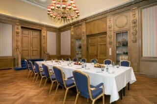 Eleganter Konferenzraum mit Holzwänden, Tisch, blauen Stühlen und frischem Obst.