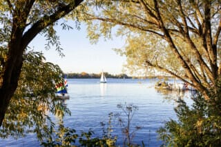 Hotel Atlantic Segelboot auf ruhigem Wasser, umgeben von Bäumen und bunten Flaggen im Herbst.