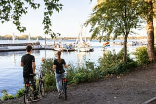 Hotel Atlantic Couple with bicycles on the shore, view of sailing boats and calm water in the background.
